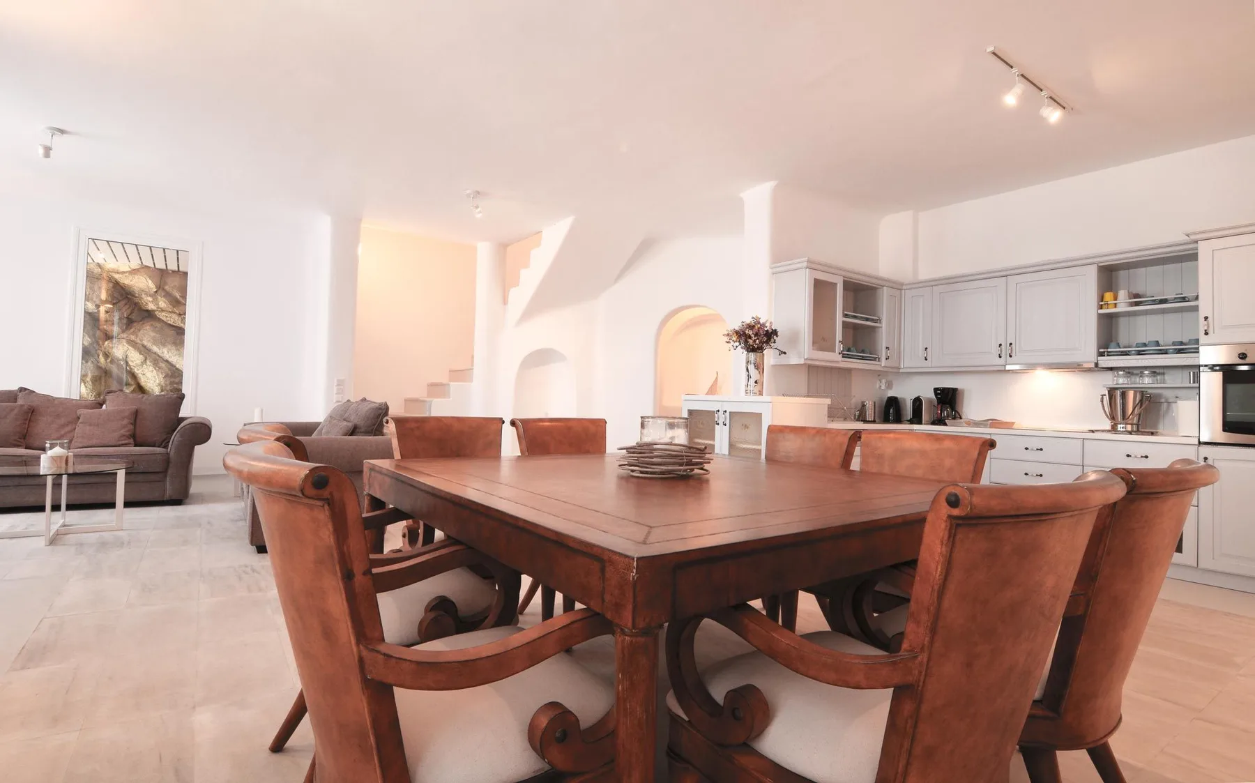 A dining area with a large wooden table and kitchen in the background.