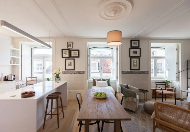A bright open-plan dining and kitchen area with a long wooden table and large windows.