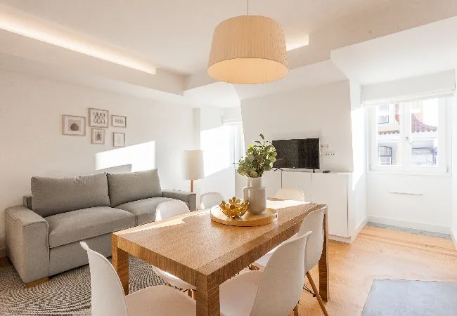 A bright living and dining area with a gray sofa and wooden table.