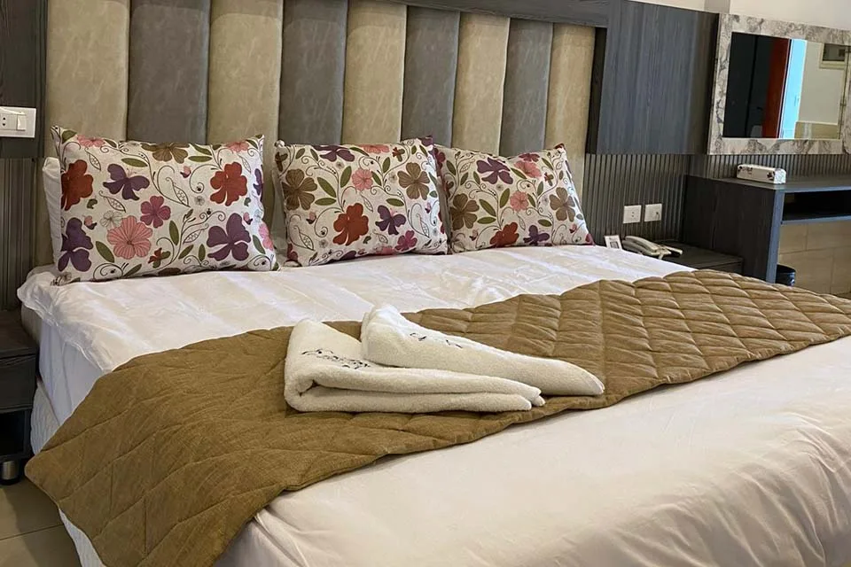 Espacio representativo del hotel: Un dormitorio con una cama adornada con almohadas florales y una colcha marrón.