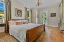 Representative hotel space: A bedroom with a wooden bed, pale bedding, and tall windows.