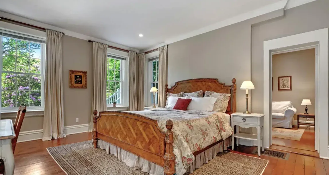 Representative hotel space: A bedroom with a wooden bed, bedside tables, and tall curtained windows.