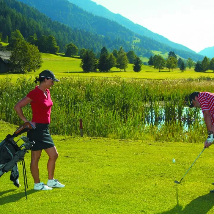 A golf course beside a marshy pond, with golfers playing on the green.