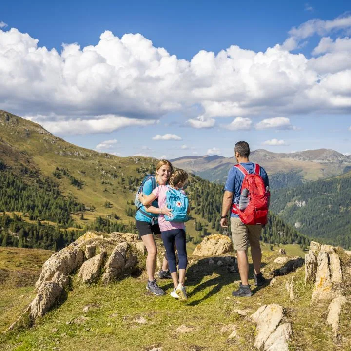 Hikers pause on a rocky mountain trail overlooking a green valley beneath a cloudy sky.