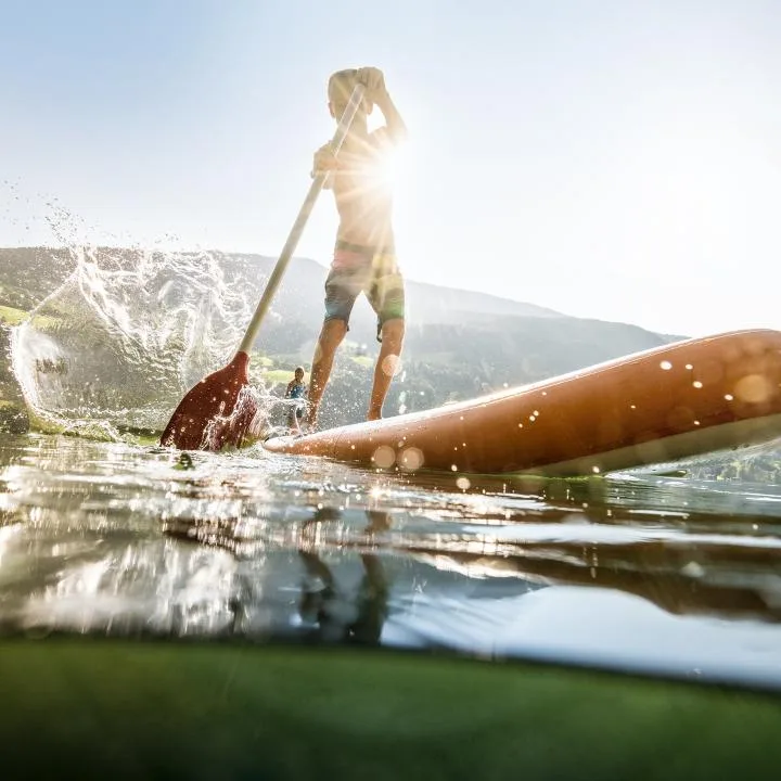 A person paddles a board across a lake with mountains in the background.