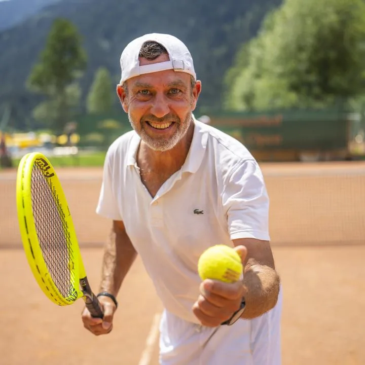 A man holds a tennis ball and racket on an outdoor tennis court.