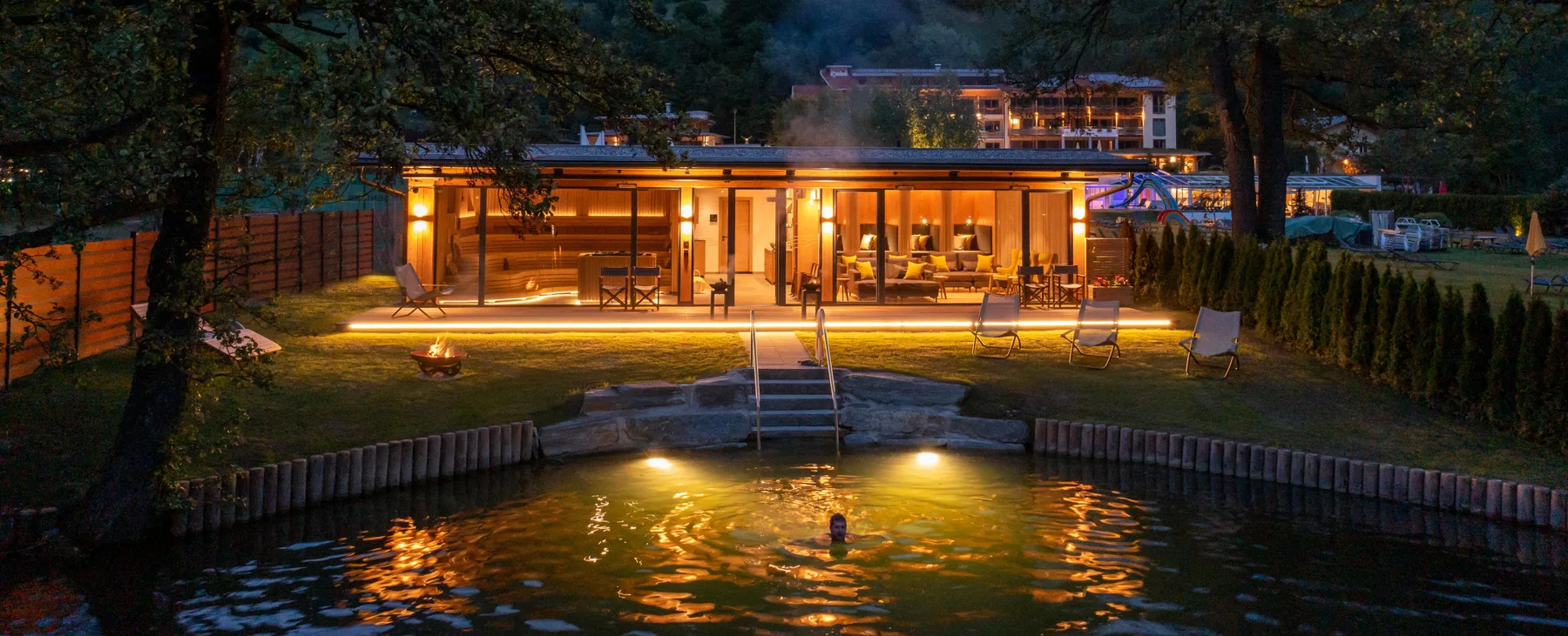 An illuminated lakeside building overlooks a small dock and the water at night.