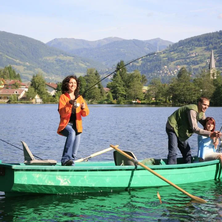 People fish from a green boat on a lake, with wooded hills in the background.