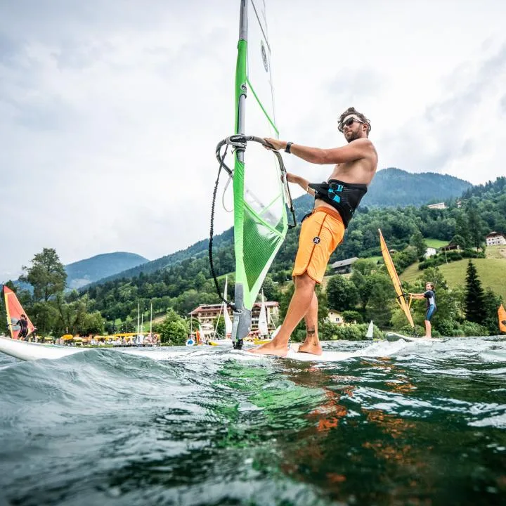 A man windsurfing on a lake, with green hills in the background.