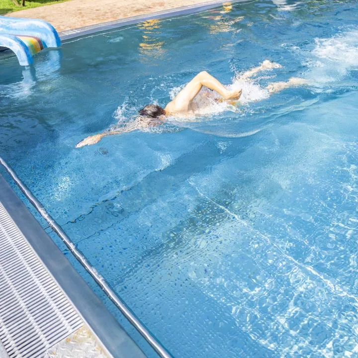 A swimmer moves through a blue outdoor pool beside the pool deck.