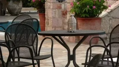 Espacio representativo del hotel: Asientos en un patio exterior rodean una mesa redonda junto a plantas con flores.