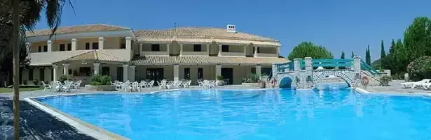 Espacio representativo del hotel: Una piscina al aire libre está junto a un edificio hotelero y un pequeño puente arqueado.