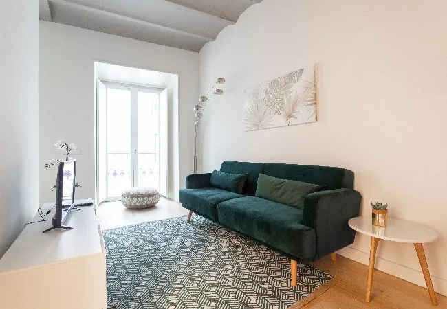 Un salón luminoso con un sofá verde oscuro junto a una ventana grande.