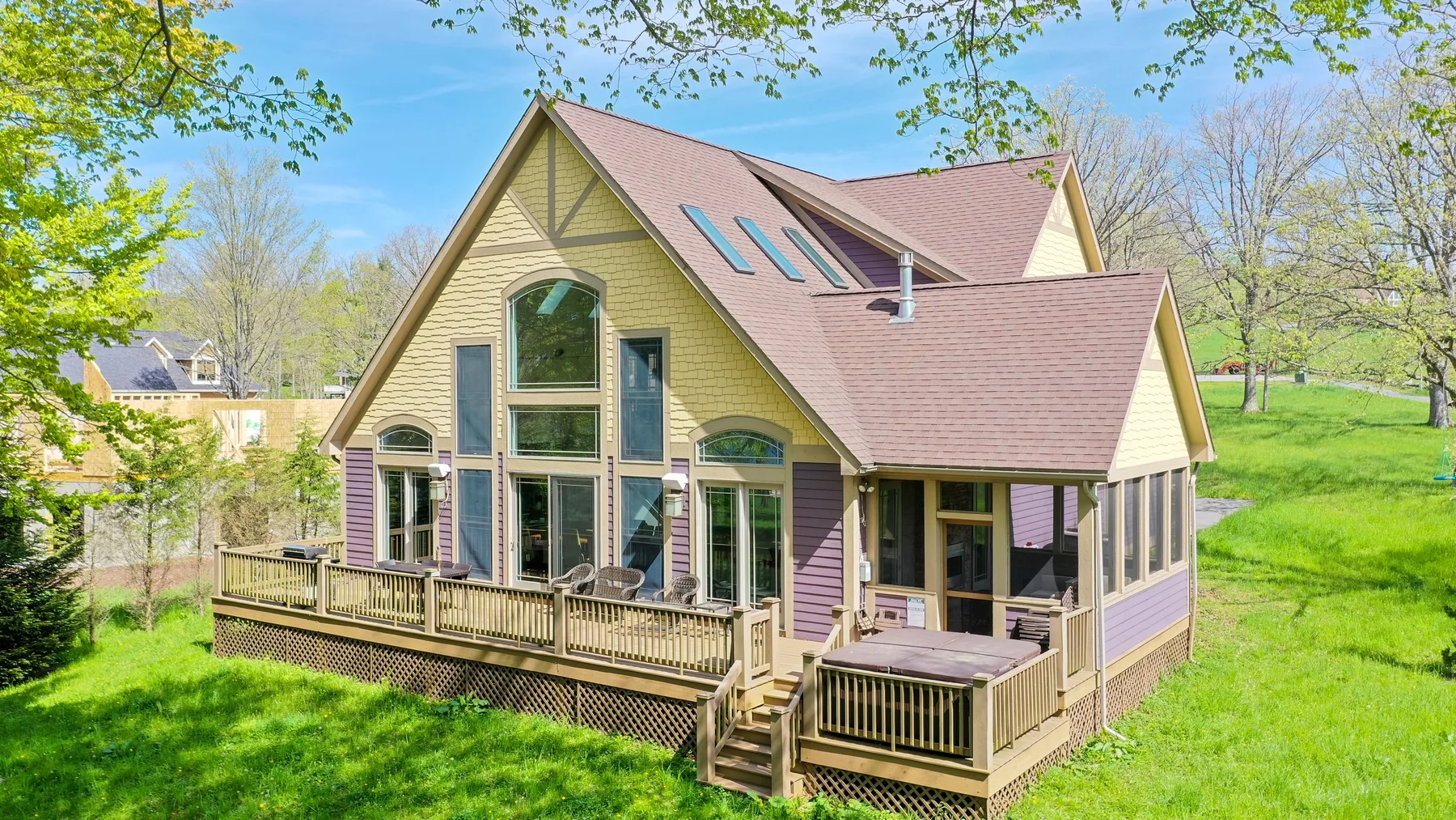 A large house with a steep roof and a raised wooden deck in a green yard.