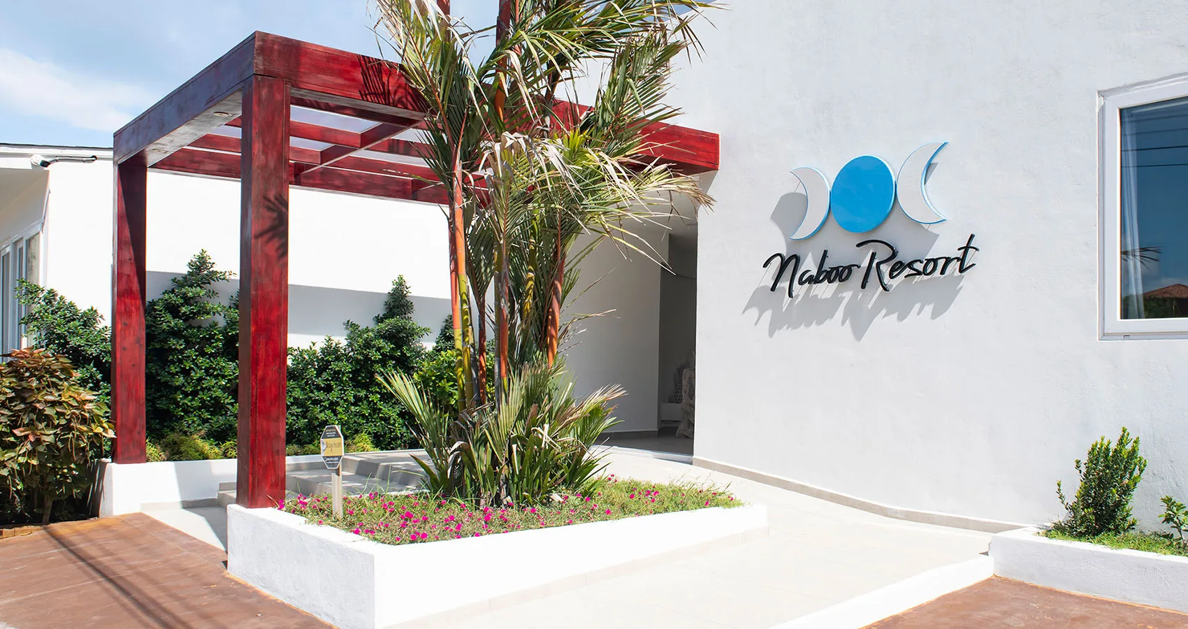 Espacio representativo del hotel: Una zona de entrada exterior con una pérgola roja y plantas.