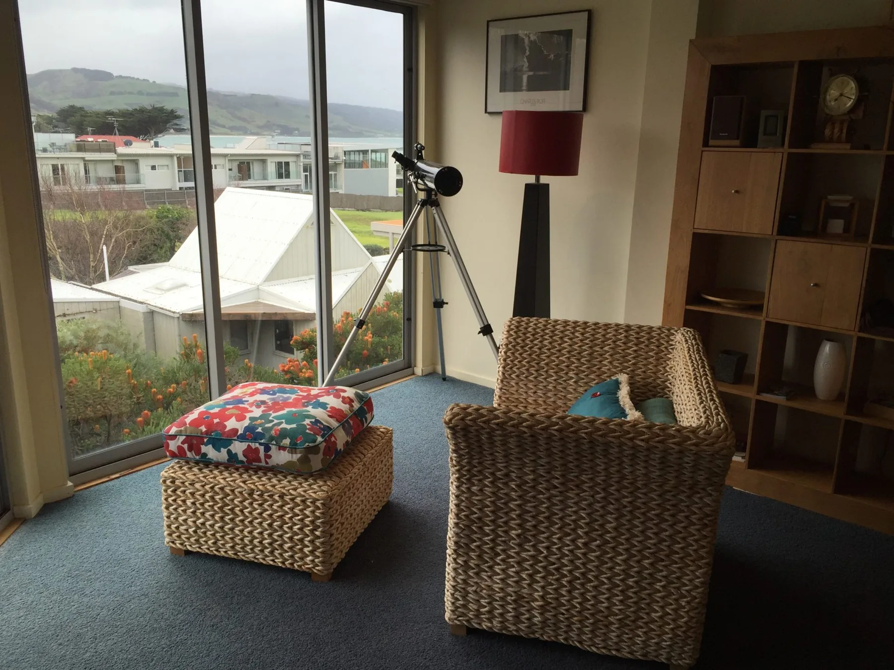 A sitting area with woven seating and a telescope beside large windows.