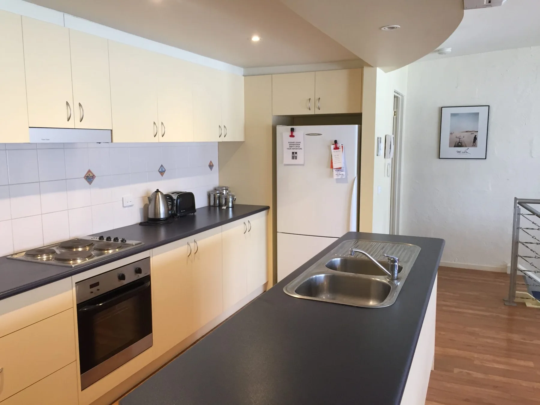 A kitchen with pale cabinets, a dark countertop, and a central island with a sink.