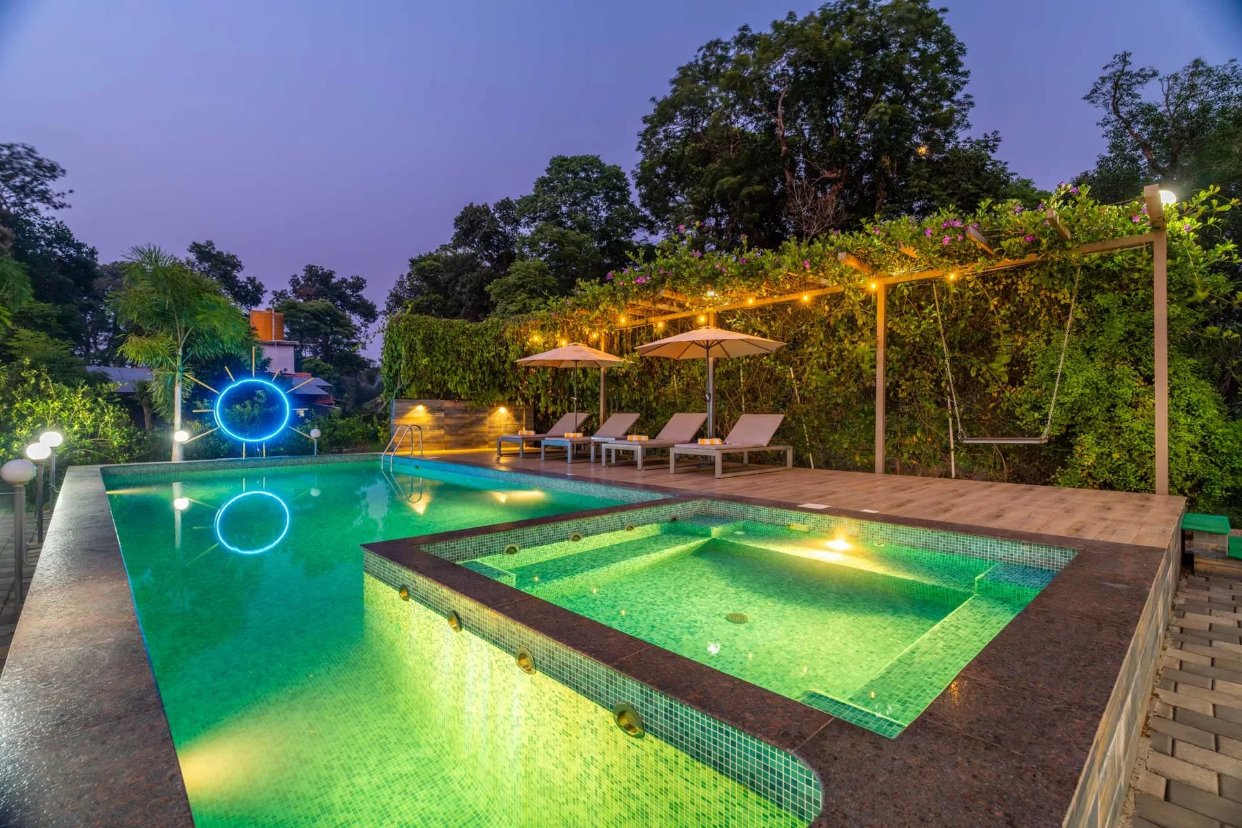Una piscina al aire libre brilla bajo las luces del jardín, con tumbonas junto a la terraza.