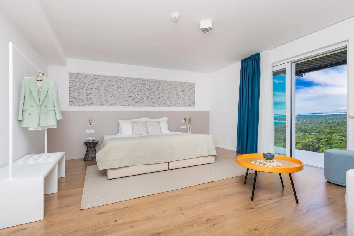 Representative hotel space: A bright bedroom with a bed beside floor-to-ceiling windows overlooking greenery and water.