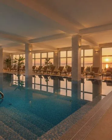Representative hotel space: An indoor swimming pool reflects sunset light through large windows.