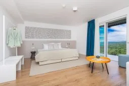 Representative hotel space: A bright bedroom with a bed, bedside table, and large windows.