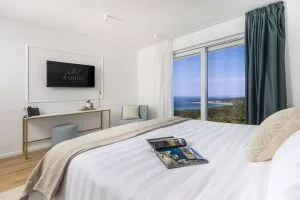 Representative hotel space: A bright bedroom with a bed facing a window overlooking the coastline.