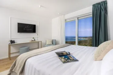 Representative hotel space: A bright bedroom with a bed beside a large window overlooking the sea.