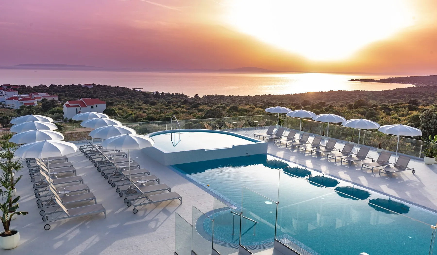Representative hotel space: A rooftop pool overlooks the sea at sunset, with rows of lounge chairs around it.