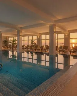 Representative hotel space: An indoor pool reflects large windows and seating at sunset.