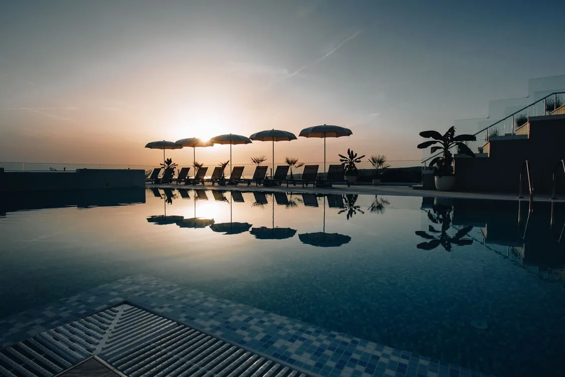 Representative hotel space: An outdoor swimming pool reflects the sunset, with umbrellas and seating along the far edge.