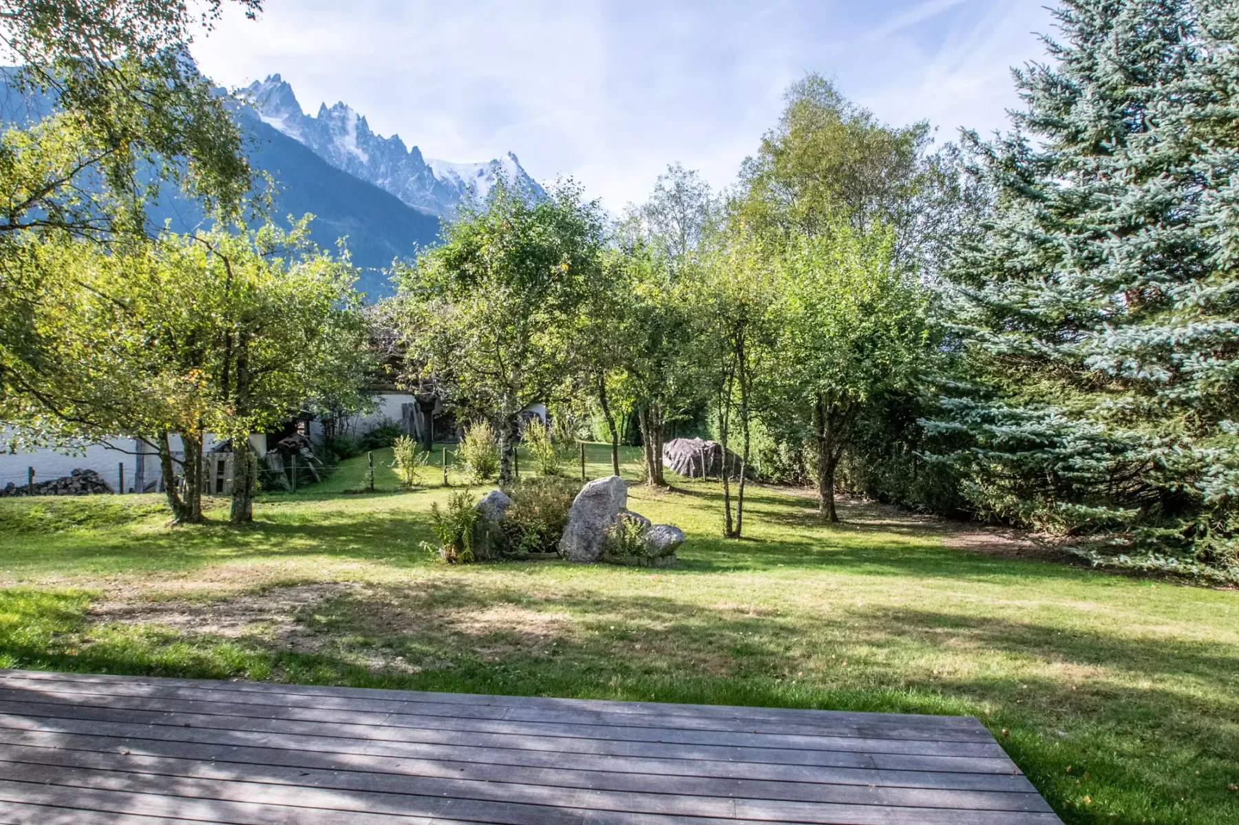 Un jardín arbolado con rocas, con picos montañosos al fondo.