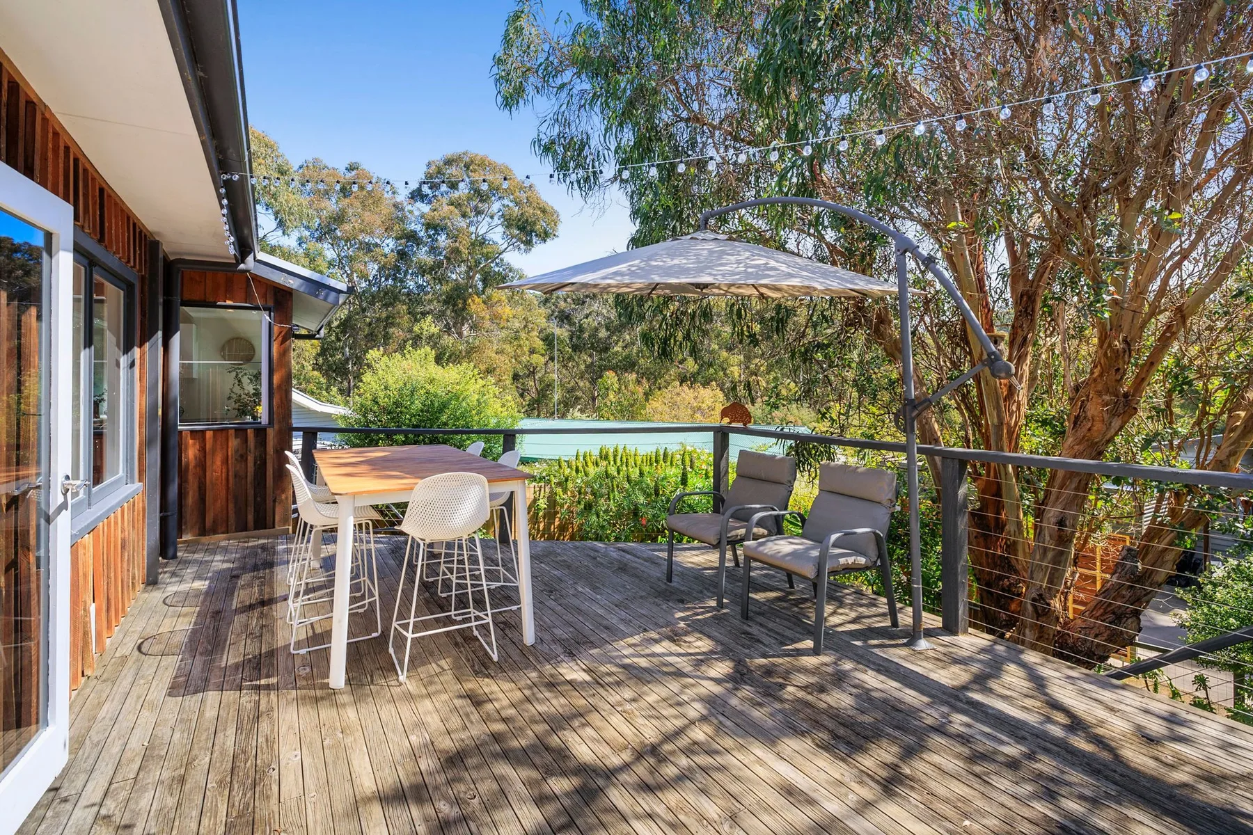 A wooden outdoor deck has a dining table, chairs, and a shaded seating area.