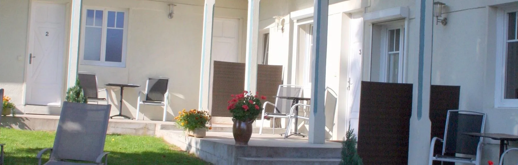 Representative hotel space: A covered patio with outdoor seating, potted flowers, and a strip of lawn.