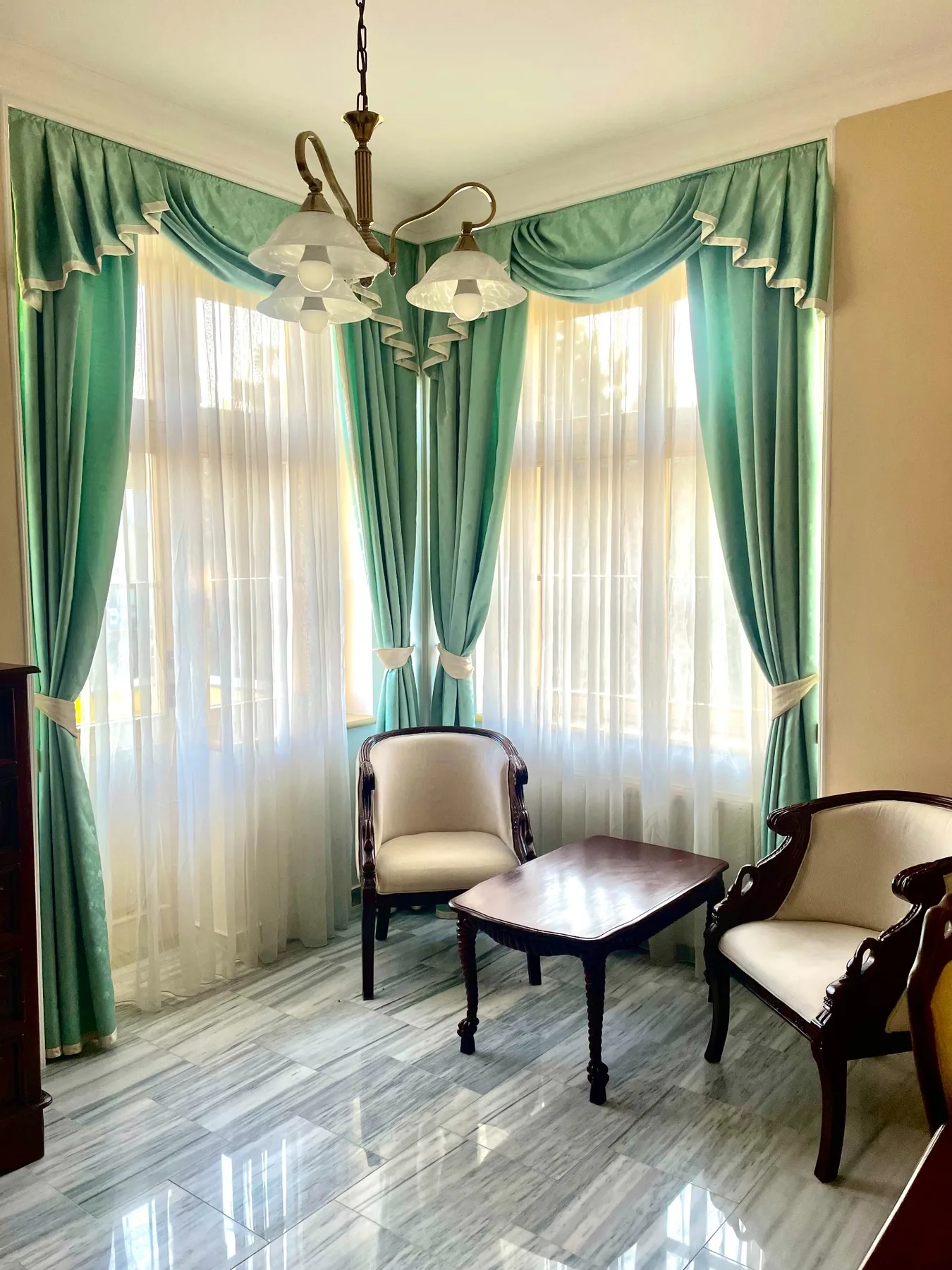 Espacio representativo del hotel: Una zona de estar con dos sillones, una mesa pequeña y ventanas altas con cortinas.