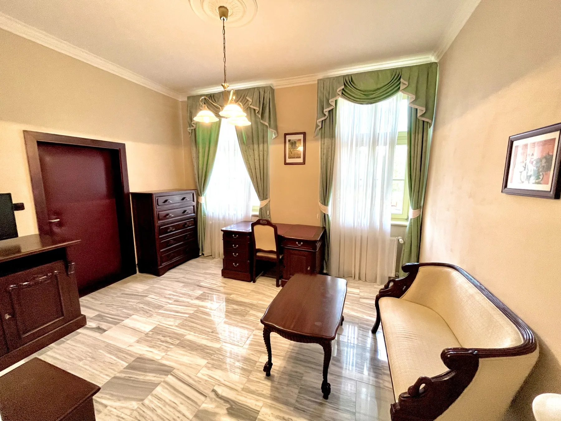 Representative hotel space: A furnished room with green curtains, wooden furniture, and a cream-colored settee.