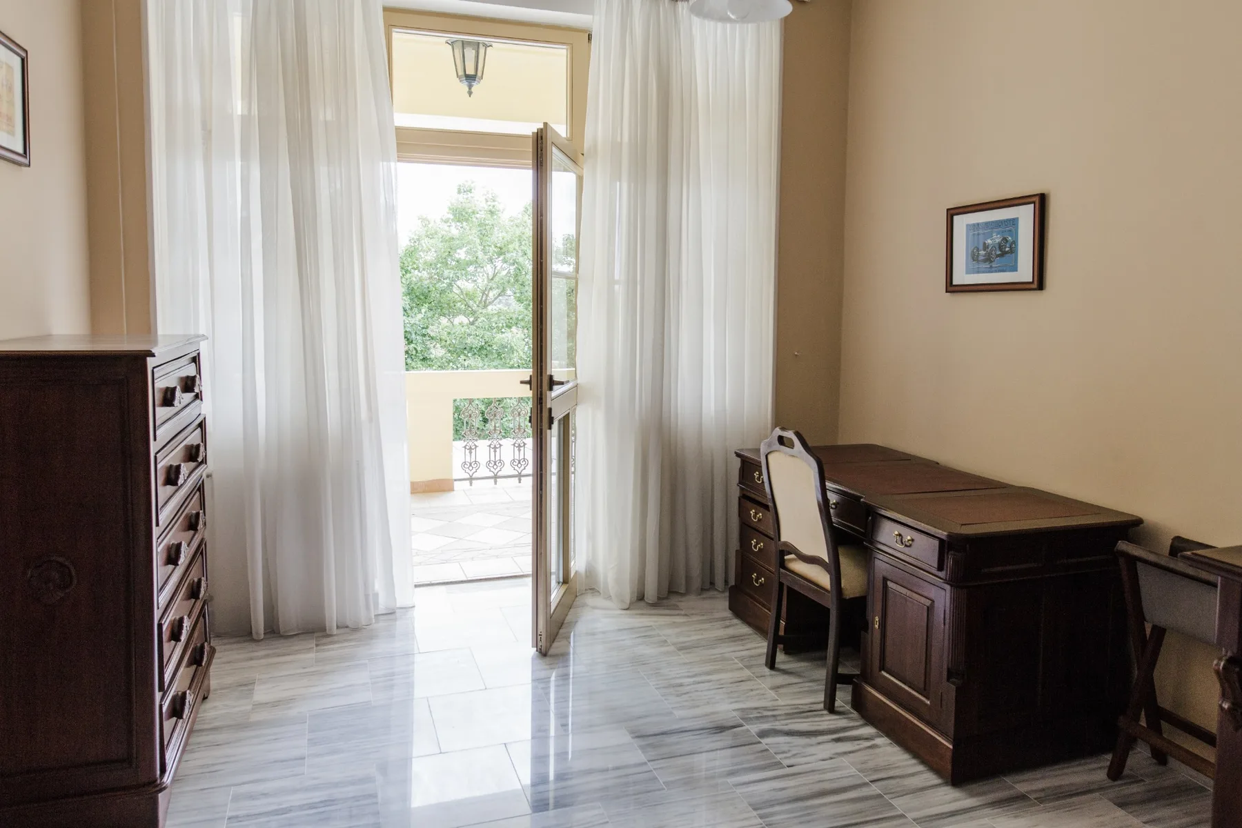 Espacio representativo del hotel: Una habitación amueblada con un escritorio junto a una puerta abierta hacia un balcón.