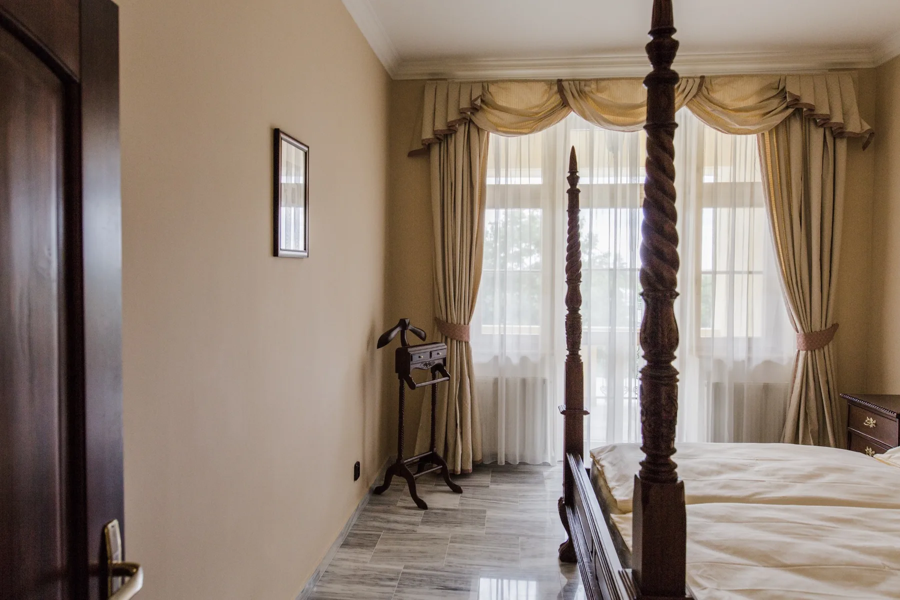 Representative hotel space: A bedroom with a tall four-poster bed beside curtained windows.