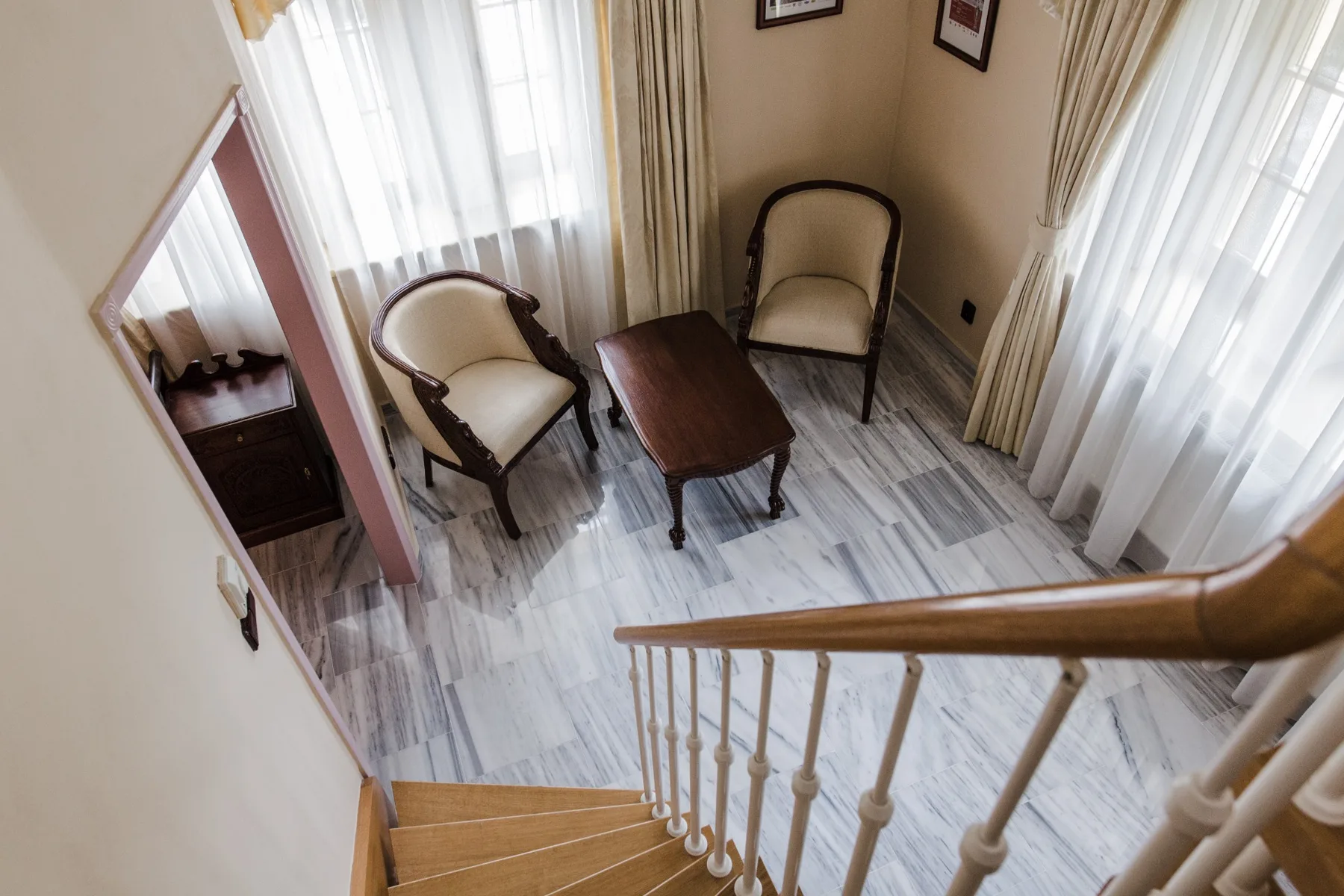 Espacio representativo del hotel: Una zona de estar con dos sillas y una mesa de centro de madera junto a ventanas altas.