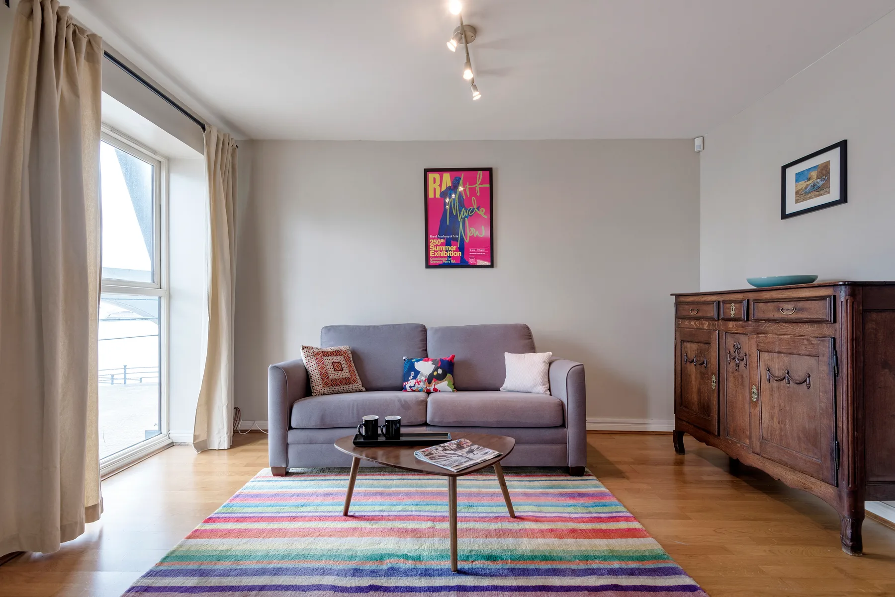 A living room with a gray sofa and a colorful rug by the window.