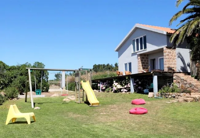 Una casa y un jardín con columpios y un tobogán sobre el césped.