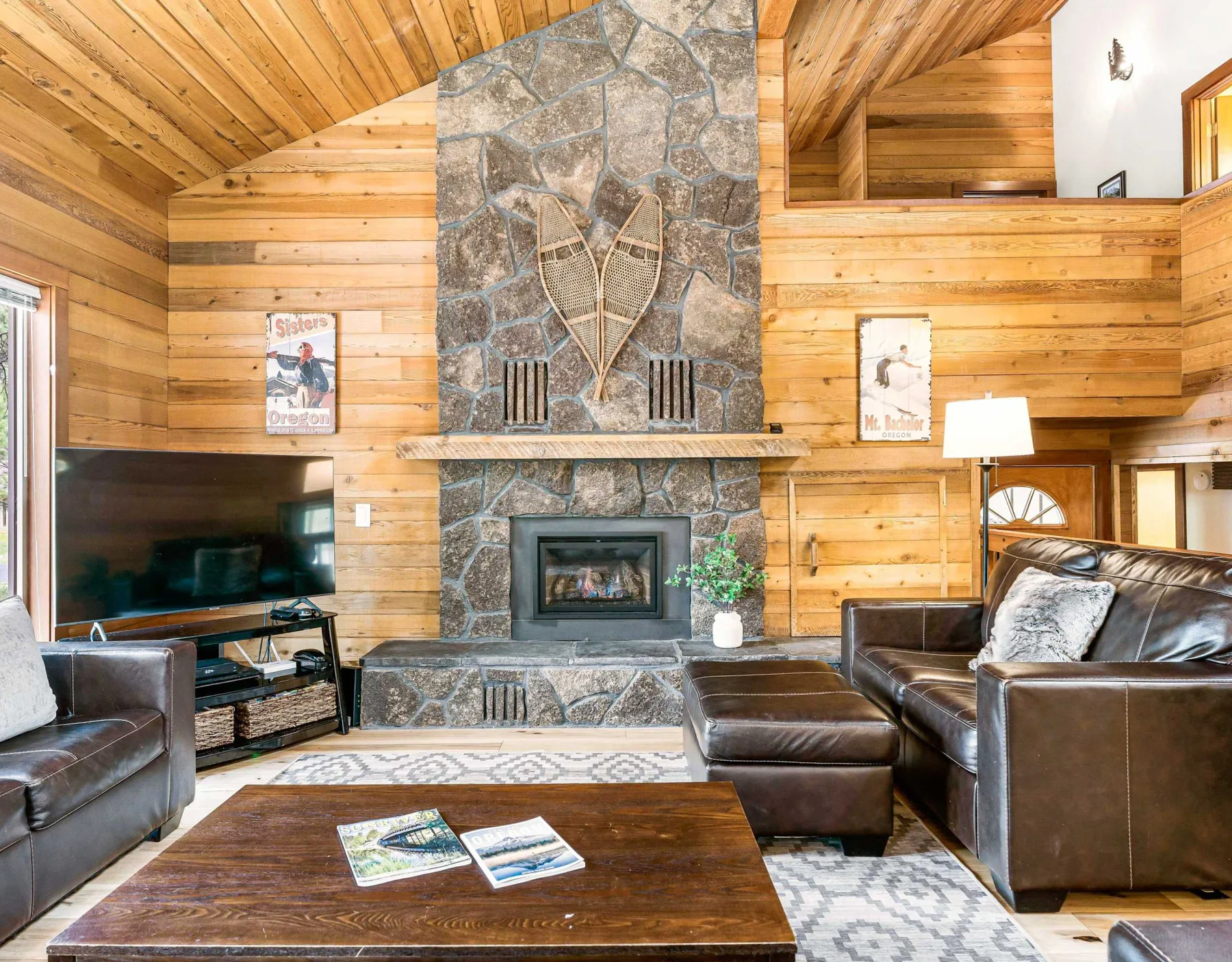 A wood-paneled living room centers on a stone fireplace, with seating and a television.