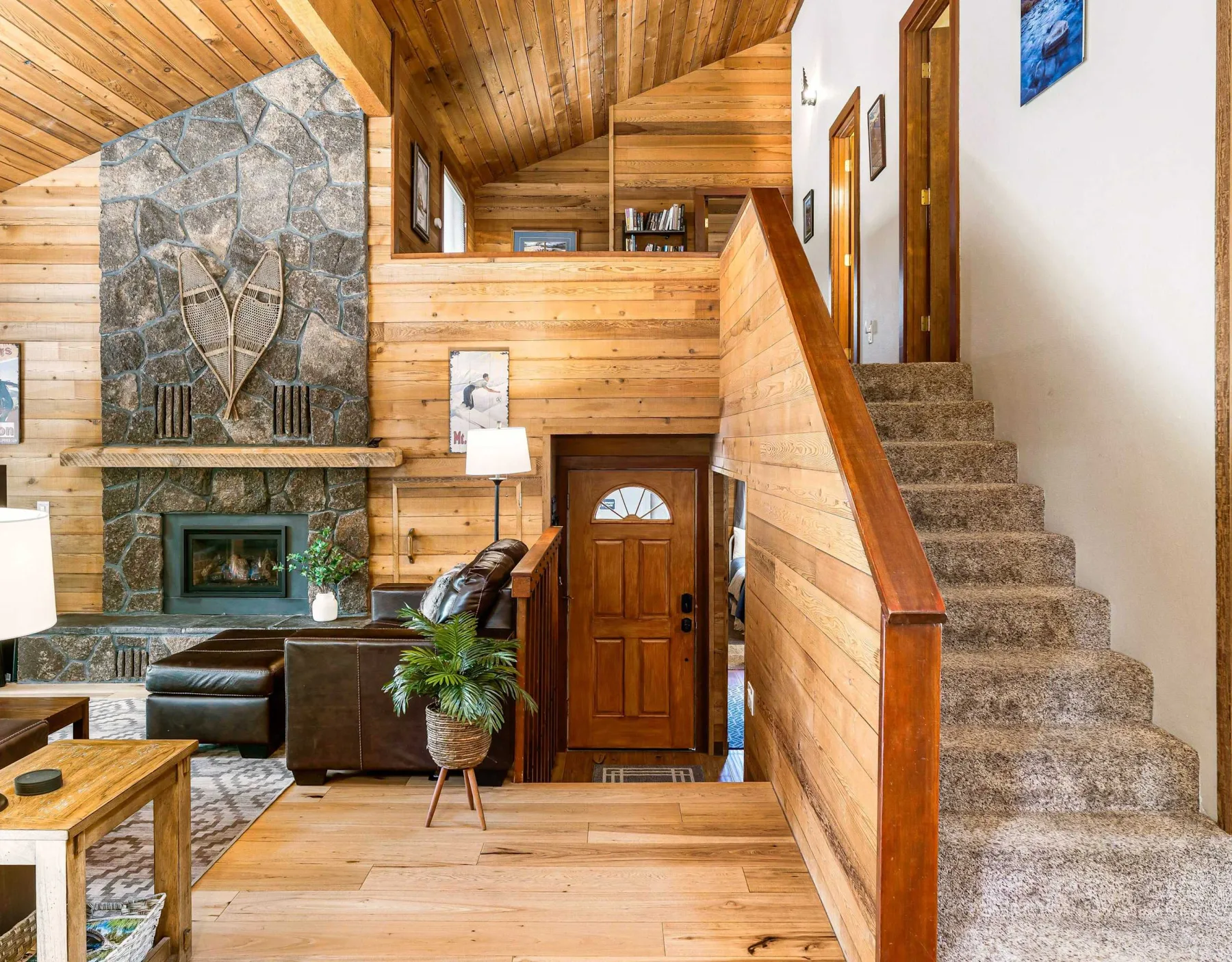 A wood-paneled living room and entry area with a stone fireplace and staircase.