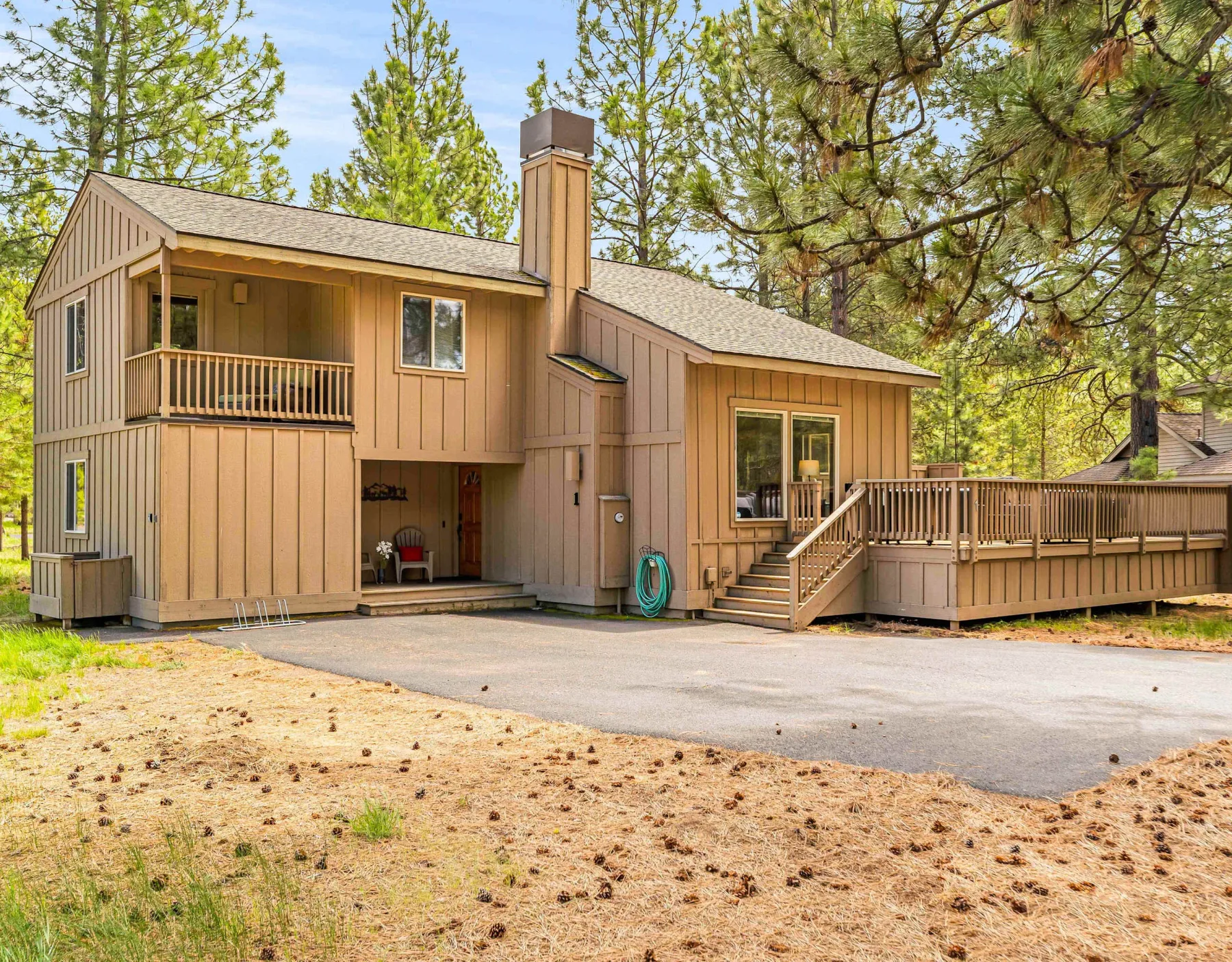 A tan house with a raised deck and surrounding pine trees.