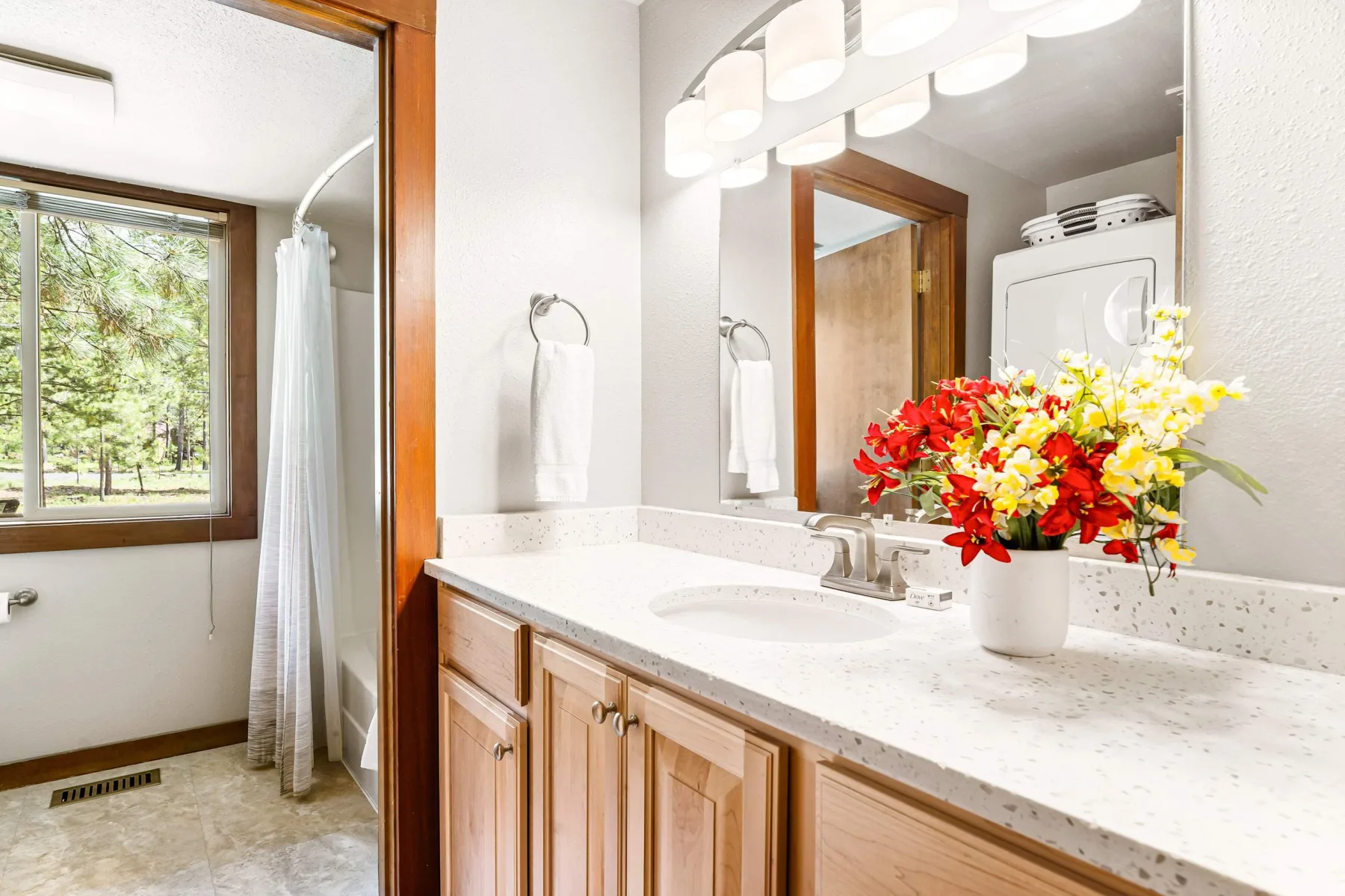 A bright bathroom with a long vanity, large mirror, and colorful flowers.