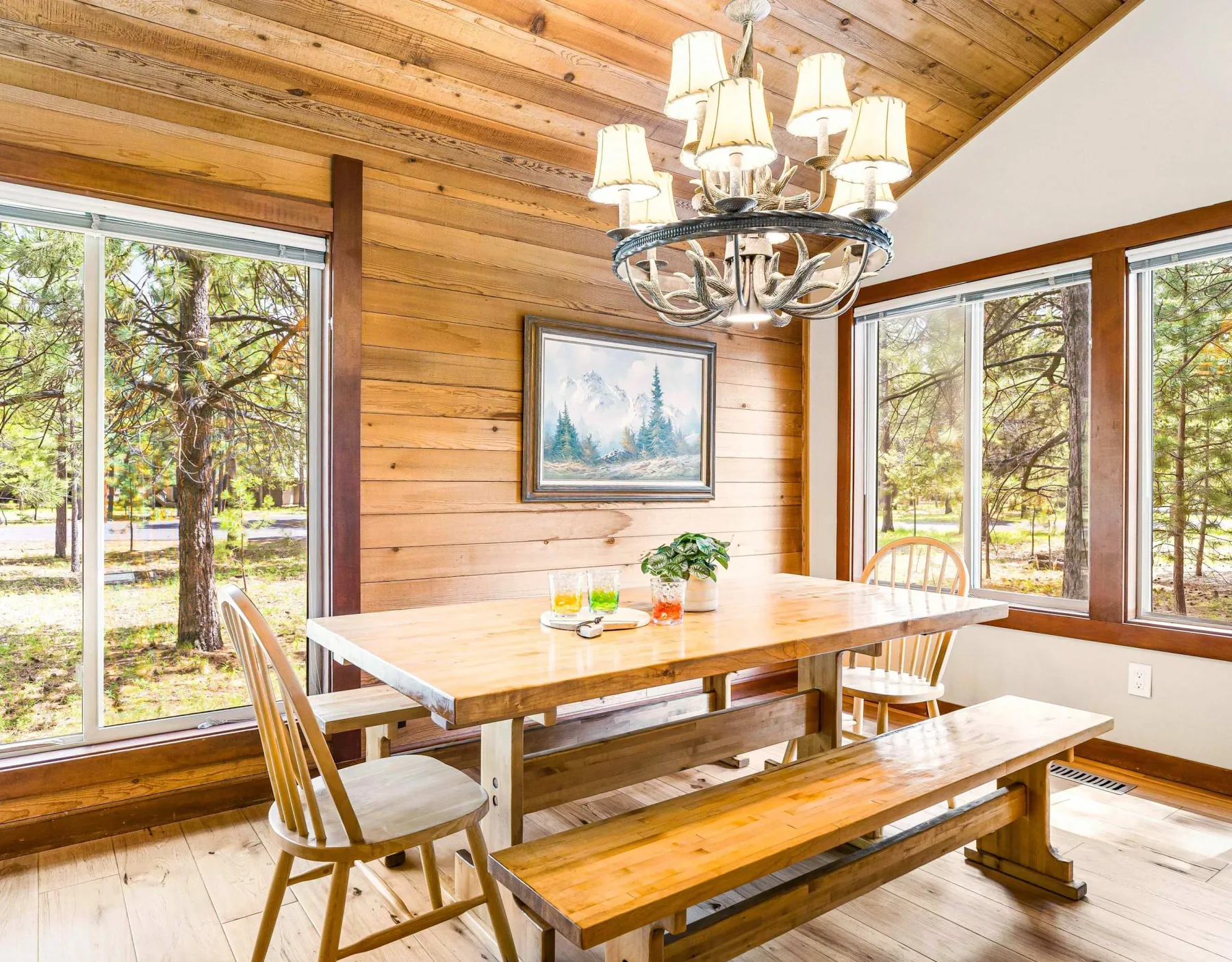 A wood-paneled dining room has a long table and bench beside large windows.