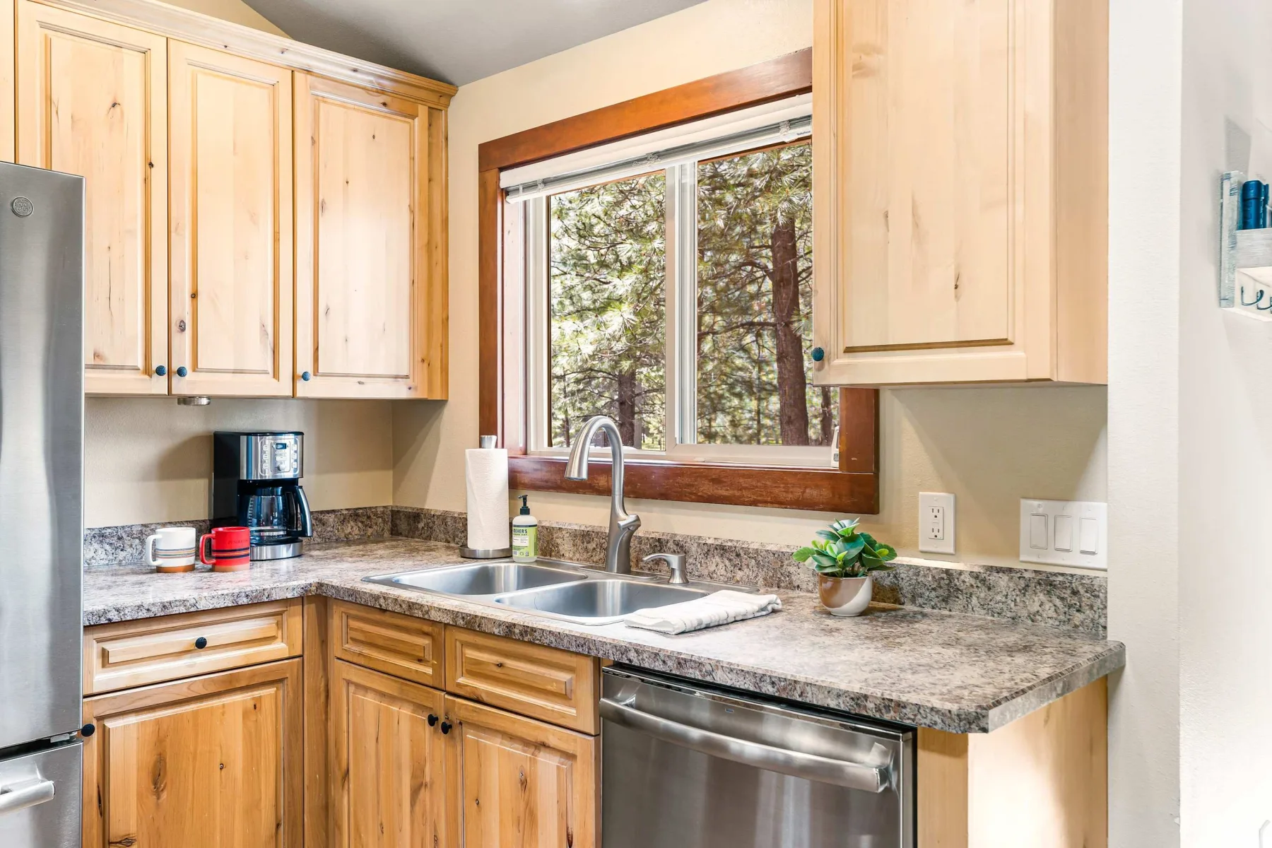 A kitchen with wooden cabinets, a sink, and a window overlooking trees.