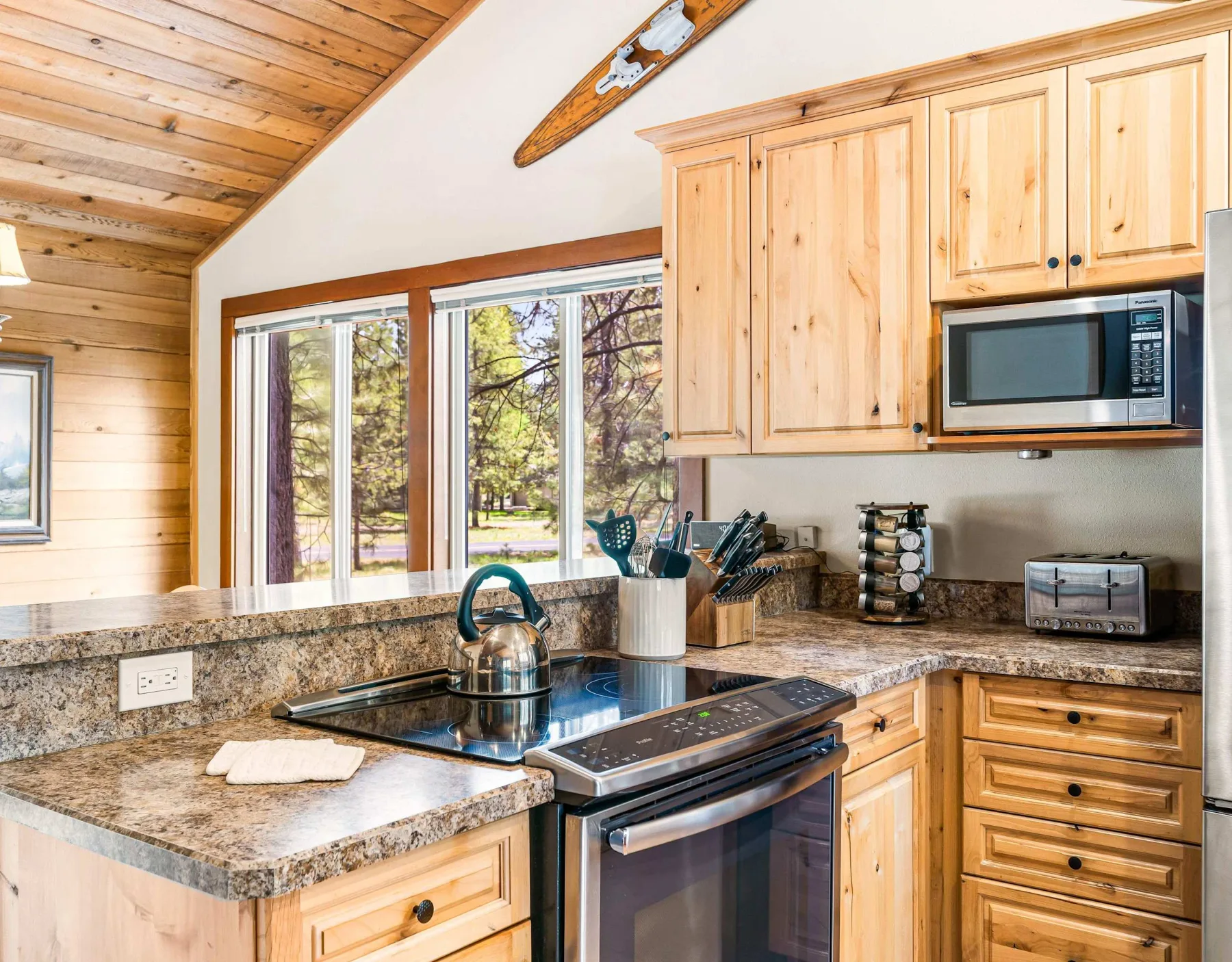A bright kitchen with wooden cabinets, stone counters, and large windows.