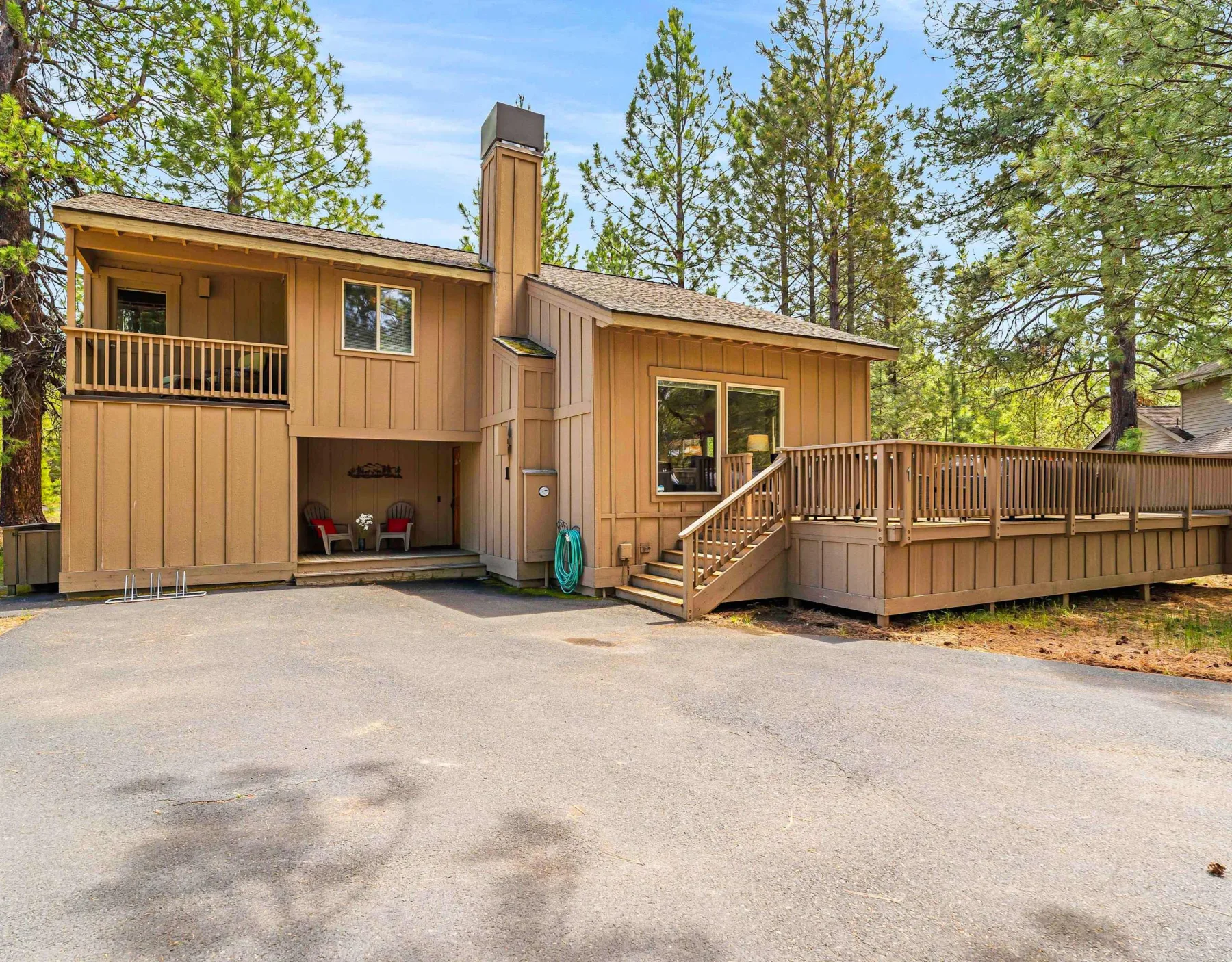 A wood-sided house stands beside a broad paved driveway, surrounded by trees.
