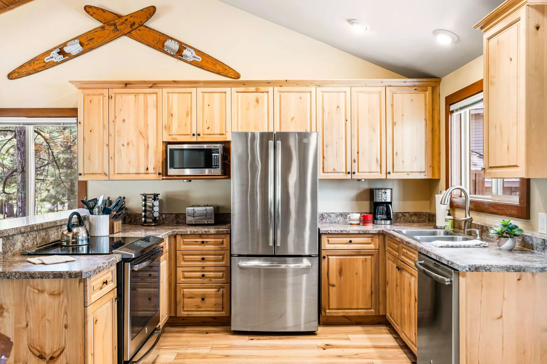 A bright kitchen with wooden cabinets, stainless steel appliances, and windows overlooking trees.