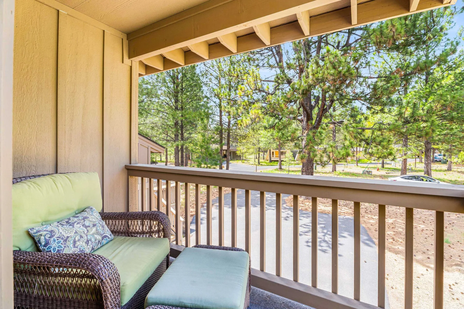 A covered porch with cushioned seating overlooks a tree-lined outdoor area.